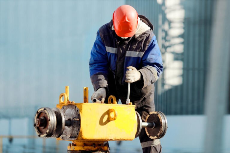 A gas service worker in a helmet and pea jacket serves a crane assembly on the street